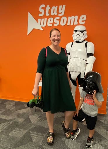 Kara standing next to a storm trooper with her son who is wearing a Darth Vader helmet