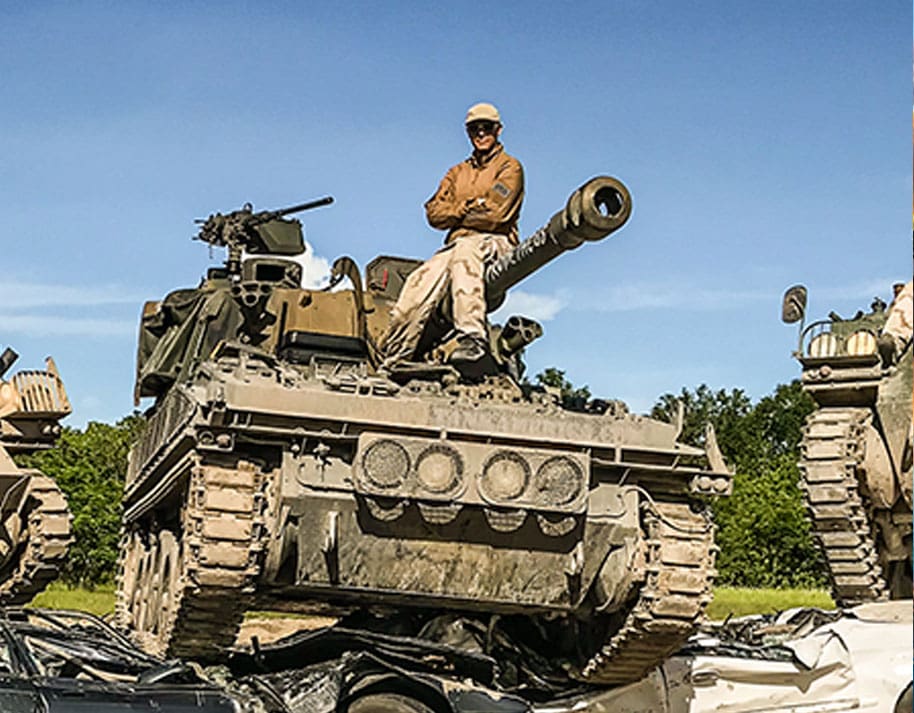 Man sitting on a tank pthat is parked atop crushed cars