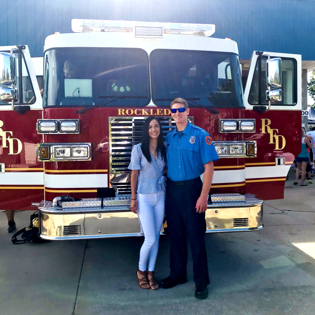 Danielle standing next to her husband in front of a fire truck parked in a fire station