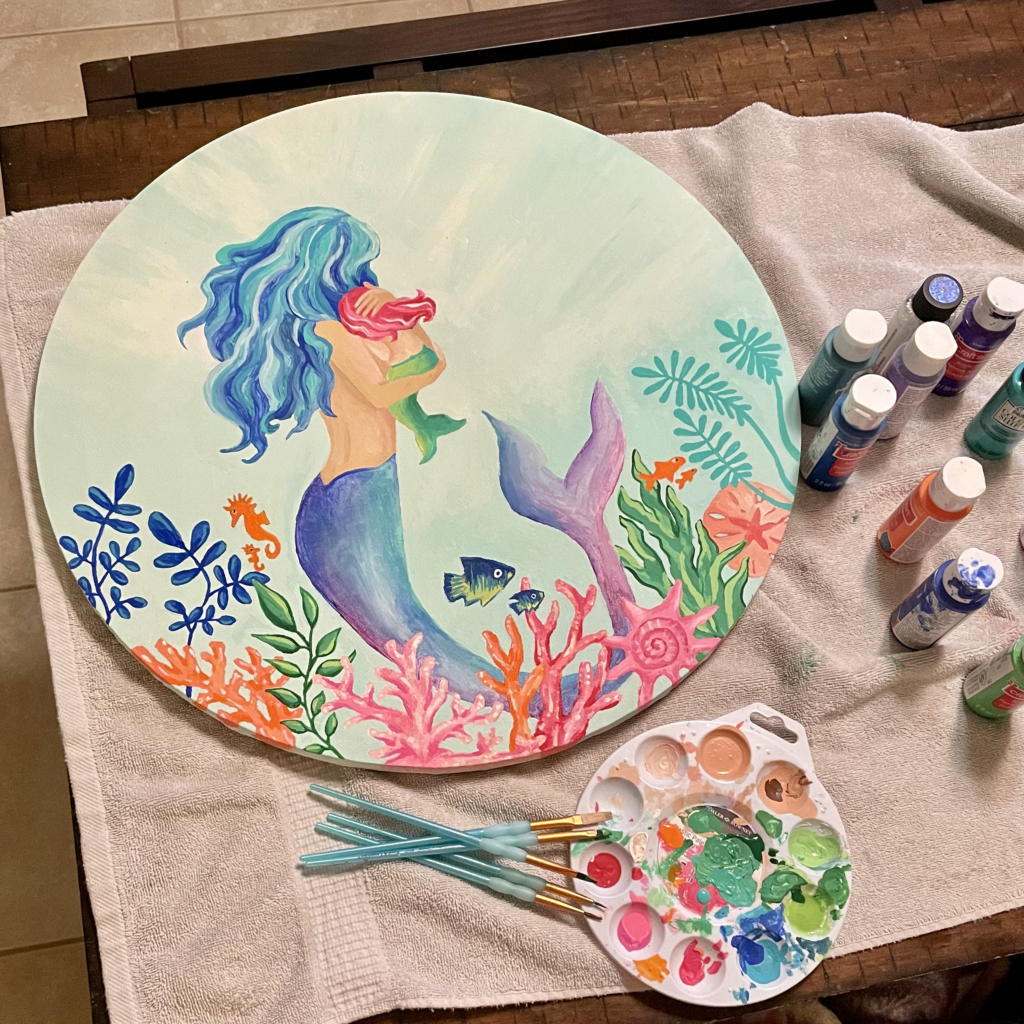 Danielle's painting of a mermaid on a round canvas with paint supplies next to it